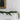 A white fireplace mantel decorated with a Norfolk pine garland and three brass candleholders with white taper candles.
