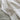 Close-up of a soft, off-white boucle throw blanket draped over a bed. The textured fabric has a plush, nubby weave and delicate fringed edges. The blanket cascades naturally over muted green bedding, creating a cozy and inviting look.