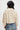 Person wearing a beige knitted sweater and blue jeans on a white background.