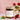 A Wild Raspberry soy wax candle in an amber glass jar with a gold lid, placed on a soft pink background. Fresh raspberries, green leaves, and a glass vase with raspberry stems surround the candle, creating a natural and cozy aesthetic