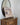 Wooden dresser with a round mirror, vase, and painting on an easel against a white wall.
