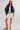 Woman wearing a denim jacket, navy cardigan, a white top, beige skirt, and tan boots on a white background.
