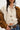 Person wearing a beige knitted cardigan over a white shirt with a brown jacket and jeans.