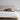 Detail shot of upholstered headboard in soft light beige polyester fabric with a brown dog laying on top of the bed.