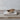Natural sandstone incense holder with a rounded, smooth design, holding two partially burned Palo Santo sticks. Displayed on a stack of aged books atop a rustic wooden surface, with a neutral-toned background.