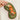 Close-up of a hand holding the Scandinavian Fox Eye Mask, showcasing the intricate embroidery of an orange fox surrounded by floral and leaf patterns on a deep green fabric background. The mask has a soft texture with a contrasting purple trim. Displayed against a neutral-colored outfit.
