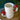 Close up of two of the Ceramic Mushroom Mugs, sitting on a round wood pedestal with one stacked on the other next to a green fern.