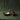A moody setting with dark green cotton drop cloth draped in background, the antique gold-finished metal bowl features a sculpted squirrel perched on the rim sits next to a couple of acorns.