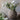 Artificial white summer garden flowers arranged in a textured, round stoneware vase against a neutral-toned backdrop, with additional flowers scattered nearby.