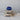 Stacked antique wooden bread boards with a bleached finish, featuring rustic handles and natural distressing. Topped with a deep blue glass vessel, creating a vintage-inspired decorative display.