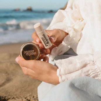 Island Coconut lip care products on a sandy beach with waves crashing in background.