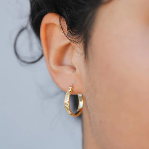 Model wearing textured golden hoop earrings. 