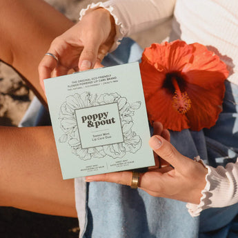 Girl holding a Sweet Mint giftbox with a red poppy on her lap. 