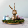 Halcyon Hare Platter with green moss and shiny easter eggs on a white marble counter. 