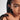 Close-up of a person wearing gold hoop earrings with braided hair on a plain background