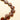 A close-up of a heart-shaped glass bead strand, showing glossy amber-brown beads with a warm golden-orange edge, arranged diagonally on a light cream background.