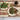 Two flatbreads with toppings on a wooden cutting board, accompanied by a jar of sauce.