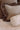 A close-up of decorative throw pillows on a bed, featuring a large beige linen pillow with a brown ruffled velvet border, a brown velvet pillow, and a cream-colored textured lumbar pillow.