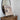 Wooden dresser with a round mirror, vase, and painting on an easel against a white wall.