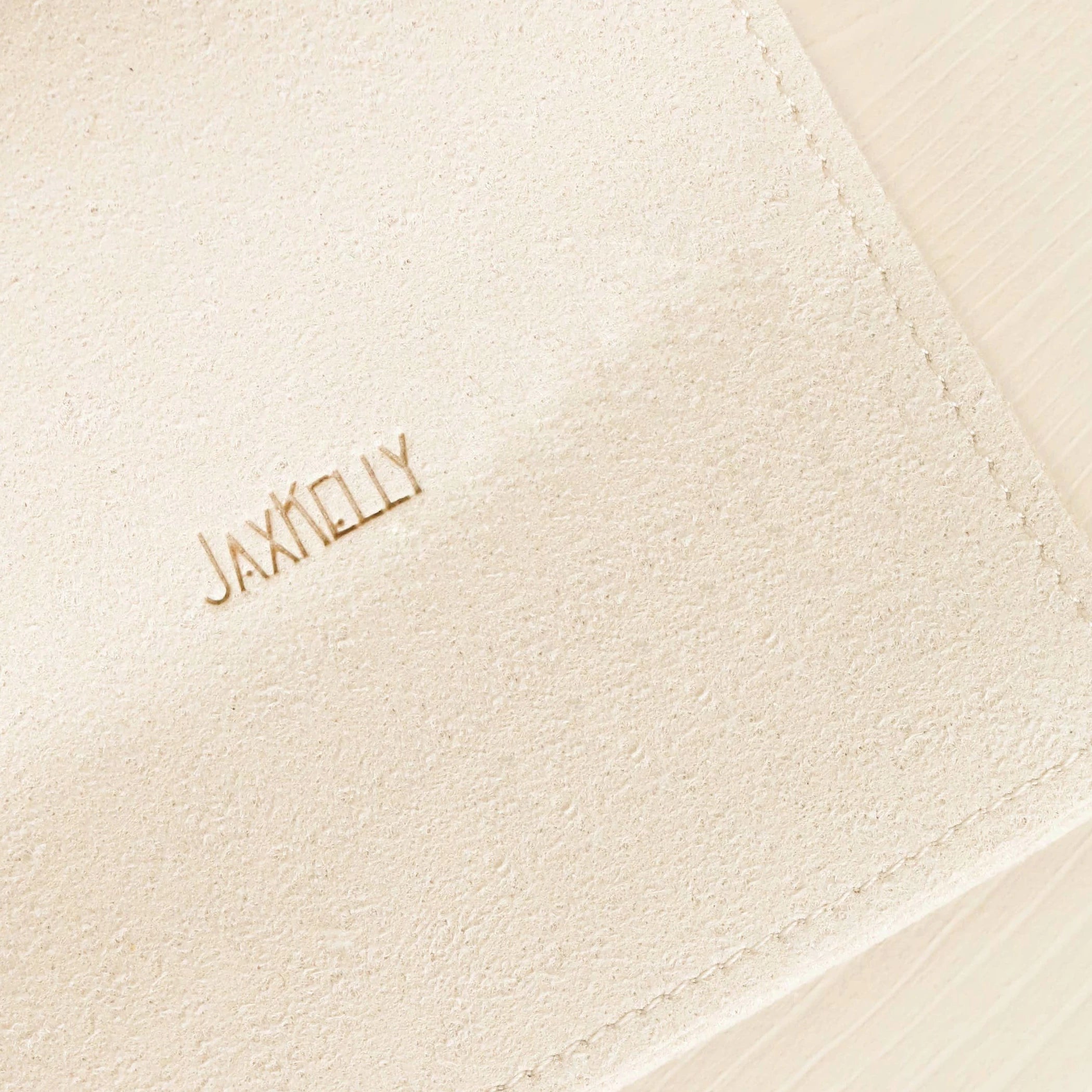 Close up view of the fabric of the JaxKelly suede-feel jewelry pouch in a cream color.