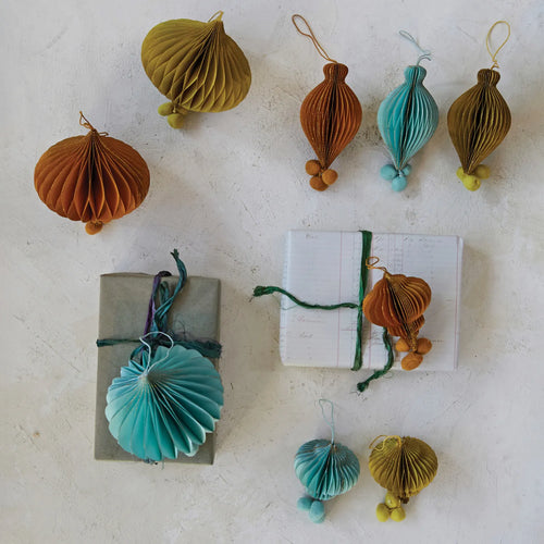 Finial ornaments in chestnut brown, blue and chartreuse with pom poms on a table with books. 