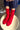 A person sitting on a stool wearing bright red ribbed crew socks with navy jogger pants, with a pair of silver shoes on the floor beside them.