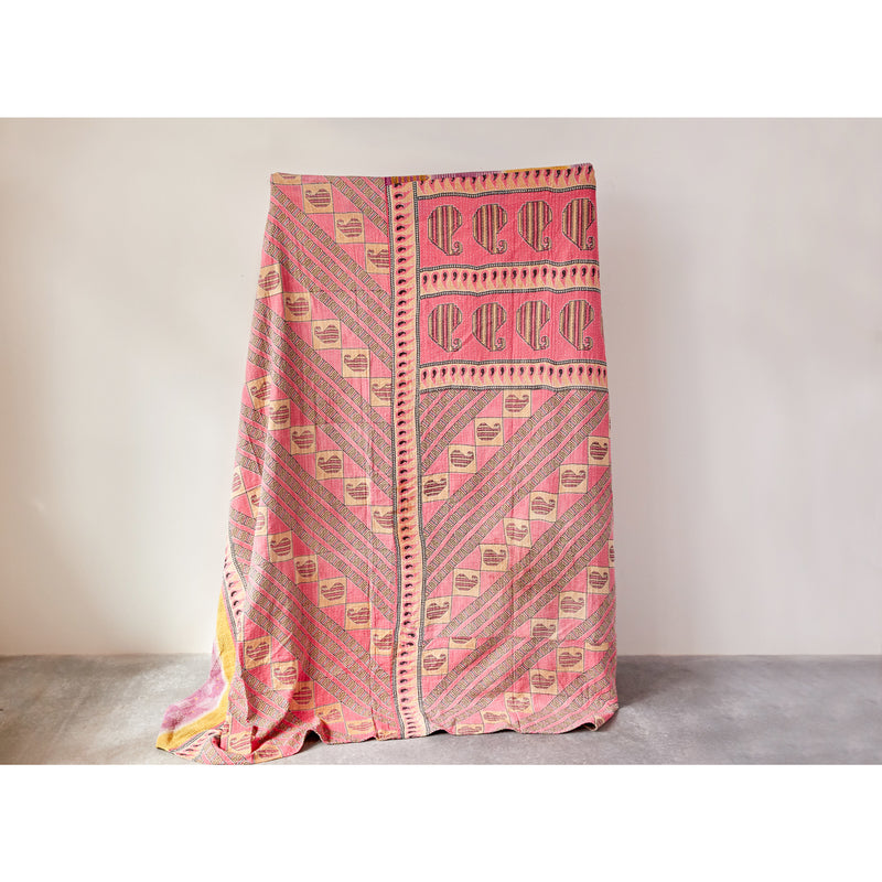 One of a kind kantha blanket being held up against a white wall. 