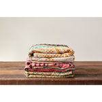 Kantha quilt blankets folded on top of a wood table. 