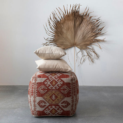 Moroccan inspired woven cotton throw cushions on a colorful floor pouf with palm leaf leaning against the wall. 