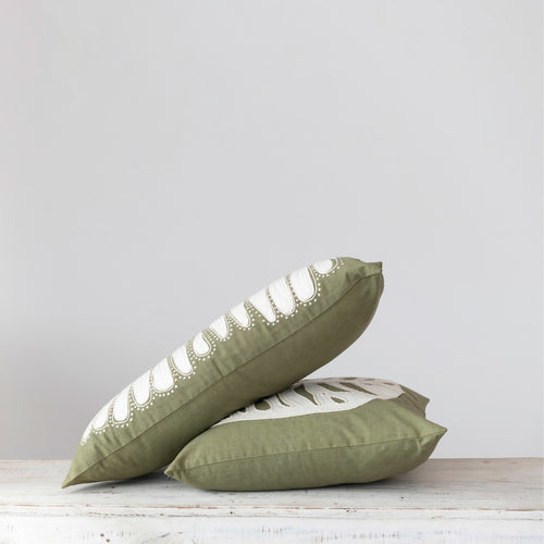 Green and cream coloured pillows stacked on a tabletop. 