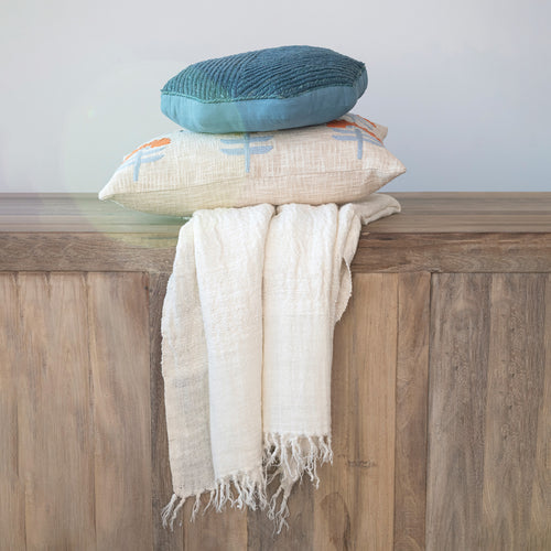 Woven Cotton Lumbar Pillow stacked with a round blue pillow and a throw blanket on a mango wood console. 