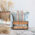20" Square Woven Linen Pillow with Stripes paired with a matching pillow and stuffed into an antique wine crate next to a basket of dried florals. 