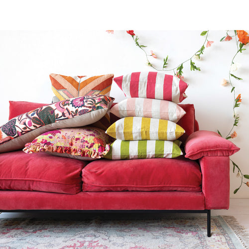 Stacks of bright coloured pillows on a hot pink velvet sofa. 