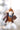 Felted mouse ornament wearing a coat and hat, holding a pine cone, against a blurred natural background.