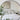 Neatly made bed with white bedding and pillows, nightstand with lamp, abstract wall art, and a plant in the foreground.