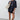 A woman modeling an oversized black t-shirt with a white teardrop graphic, paired with black shorts, black sandals, and carrying a beige shoulder bag against a light gray studio background.