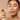 Person applying a mist spray to their face against a beige background