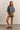 Woman wearing a blue top and brown shorts against a plain background