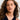 Woman with wavy hair wearing gold earrings against a neutral background.