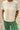 Person wearing a white t-shirt and green pants standing on sandy ground