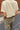 A person shown from behind wearing a cream-colored short-sleeve t-shirt and leopard print pants, standing outdoors against a brick wall and asphalt pavement.