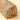 A close-up of a cylindrical fabric pouch or bag with an abstract ikat-style pattern in brown, black, and cream, featuring a braided gold tassel and tassel detail on a light beige background.