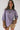 Woman wearing a layered outfit with a purple top and striped sleeves against a plain background