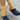 Person wearing mustard yellow socks with white stripes and navy blue clogs on a textured floor.