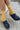 Person wearing mustard yellow socks with white stripes and navy blue clogs on a textured floor.