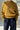 Person wearing a mustard yellow sweater and dark pants in an urban setting