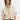 Woman wearing a beige knitted cardigan over a white shirt on a light gray background.