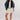 Woman wearing a denim jacket, navy cardigan, a white top, beige skirt, and tan boots on a white background.