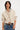 Woman wearing a beige cardigan over a white shirt with blue jeans on a white background.
