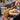 Person spreading peanut butter on bread using a jar with the long wooden spreader in a kitchen.